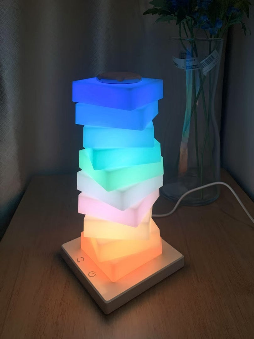 Stack of colorful square lights on a wooden surface with a plant in the background