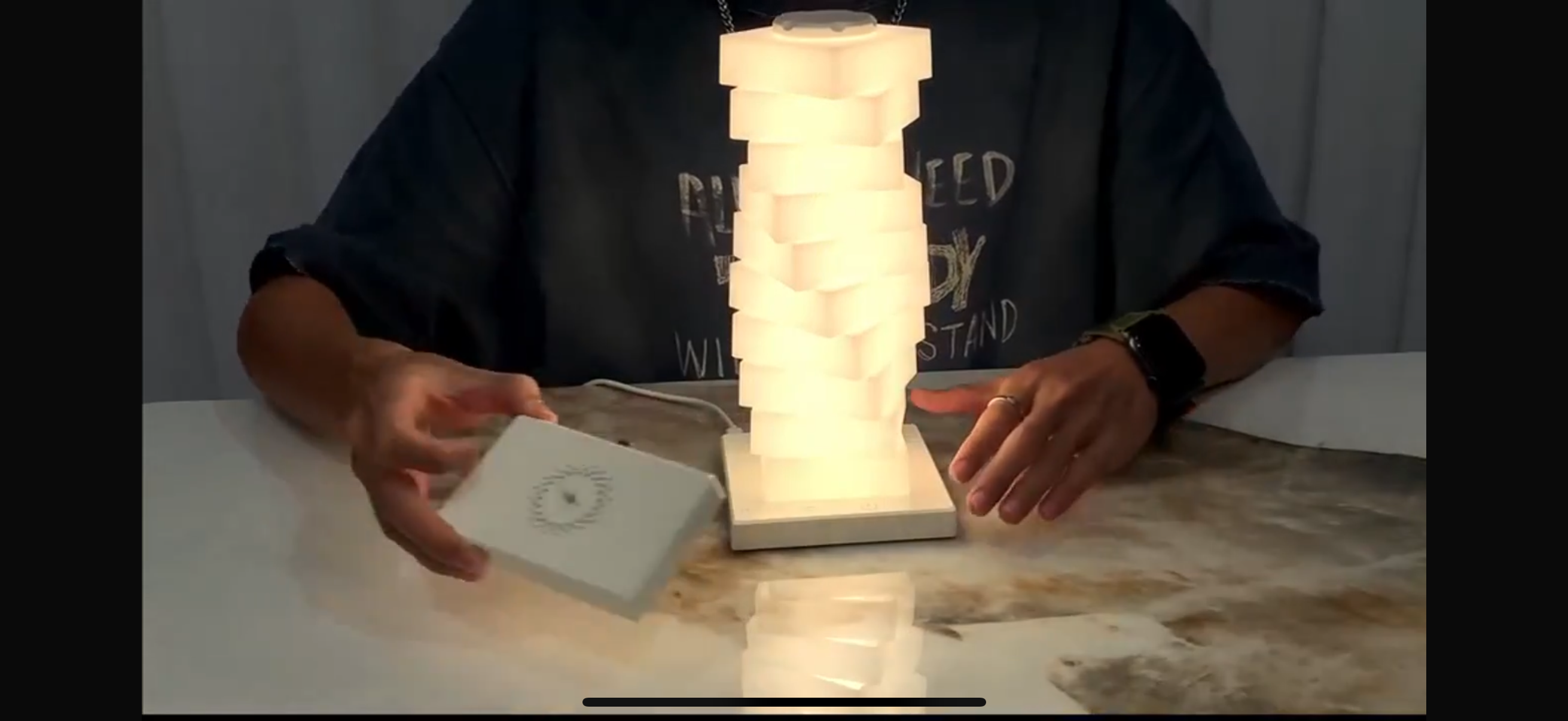 Person holding a small white device next to a stack of illuminated lamps on a table.