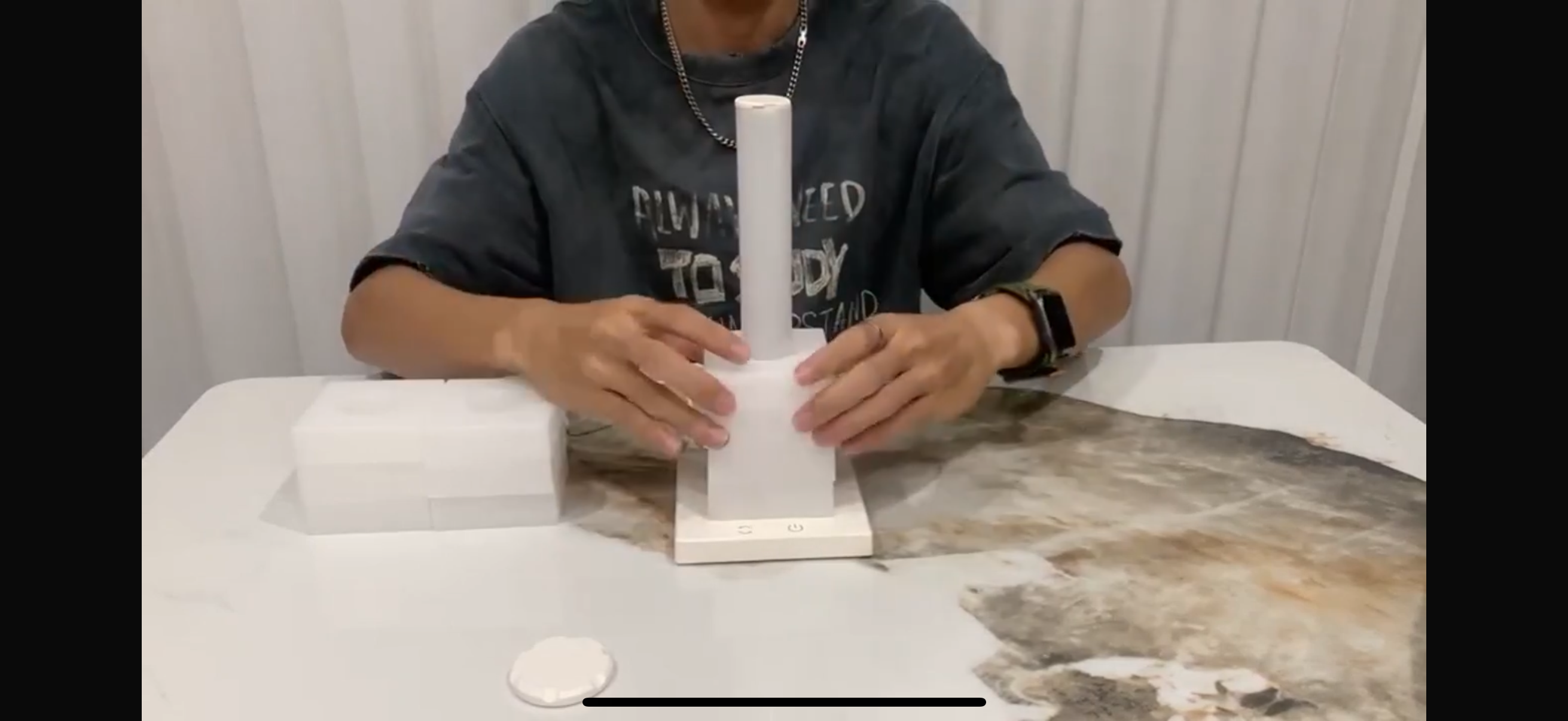 Person holding a white cylindrical object on a table with a plain background